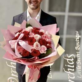 Man holding a large bouquet of red and pink roses wrapped in pink paper