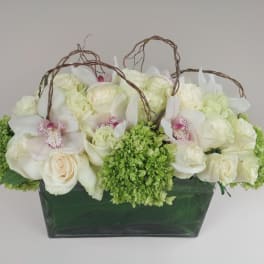 White roses and orchids arranged in a green vase with twig handles