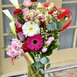 Mixed bouquet in a glass vase with roses, gerbera daisies, orchids, and calla lilies
