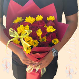 Bouquet of red roses and yellow daisies wrapped in burgundy paper