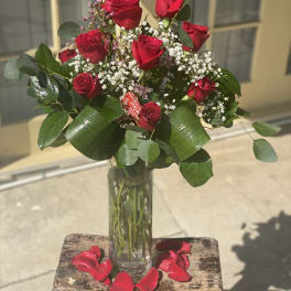Red roses in a clear glass vase with baby's breath and rose petals