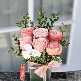 Pink roses in a glass vase with a white orchid and ribbon