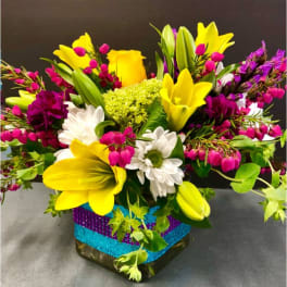 Bright mixed bouquet with yellow lilies, white daisies, and pink accents in a decorated vase