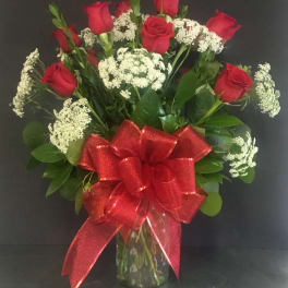 Tall arrangement of red roses and white filler flowers in a clear glass vase with a large red bow.