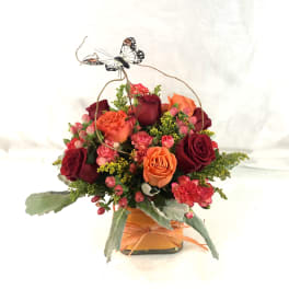 Mixed rose arrangement in a square vase with a butterfly topper
