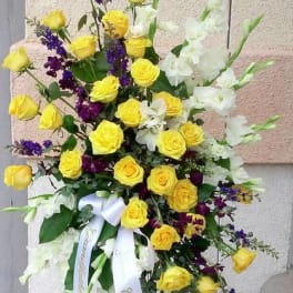 Tall standing spray of yellow roses, white gladiolus, and purple accents