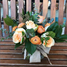Peach roses and orange blooms arranged in a clear glass vase with a burlap bow
