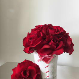 Red roses arranged in a white textured container with a gingham ribbon