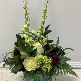 Tall floral arrangement in a teal vase with pale yellow roses and green orchids