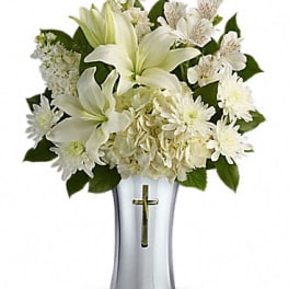 White lilies and daisies arranged in a silver vase with a cross