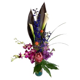 Tall tropical bouquet with orchids, calla lilies, and a protea in a glass vase