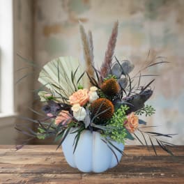 Peach roses in a white pumpkin-shaped vase with dried grasses and dark foliage