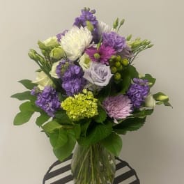 Bouquet of purple, white, and green flowers in a clear glass vase