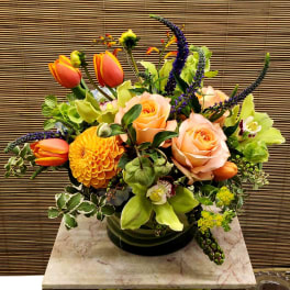 Mixed bouquet with peach roses, orange tulips, and green orchids in a glass vase