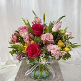 Mixed pink, yellow, and white flowers arranged in a glass vase with a ribbon