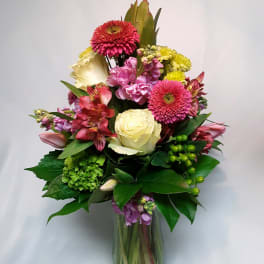Mixed bouquet in a clear glass vase with pink, cream, and yellow flowers