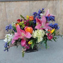 Mixed bouquet with pink lilies, roses, and blue flowers in a glass vase