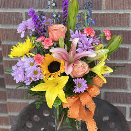 Mixed bouquet with sunflowers, lilies, roses, and purple daisies in a glass vase