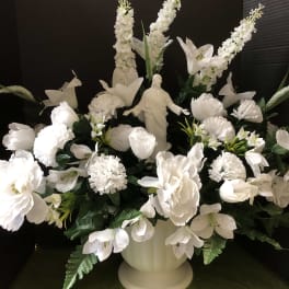 White floral arrangement with a religious statue in a pedestal vase