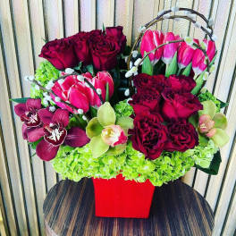 Bouquet of burgundy roses, pink tulips, and orchids in a red vase