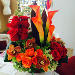 Arrangement of red roses, orange calla lilies, and orchids in a low container
