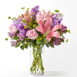 Pink lilies and roses with purple flowers in a clear glass vase