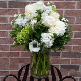 White floral arrangement in a glass vase with green accents