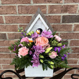 Mixed pink and purple flowers arranged in a white wooden birdhouse planter