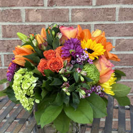 Mixed bouquet in a clear glass vase with orange, yellow, purple, and green blooms