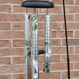 Black metal wind chime with silver tubes and bird designs hanging on a brick wall.