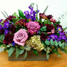 Mixed bouquet with pink roses and purple flowers in a rectangular wooden container