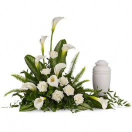 White calla lilies and roses in a low arrangement beside a white urn