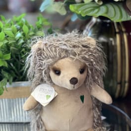 Plush hedgehog toy with a tag, displayed among potted flowers
