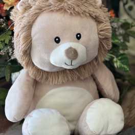 Plush teddy bear with a tan mane sitting in front of flowers
