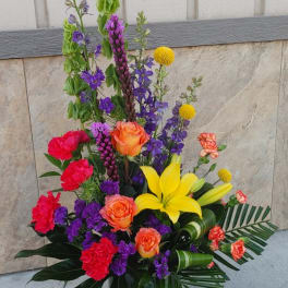 Tall mixed flower arrangement in a dark vase with yellow lilies and orange roses