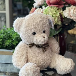 Teddy bear in front of a floral arrangement with pink and cream roses