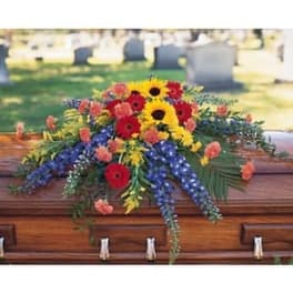 Colorful funeral casket spray with sunflowers, gerbera daisies, and blue flowers