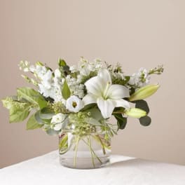 White lilies and small white flowers arranged in a clear glass vase
