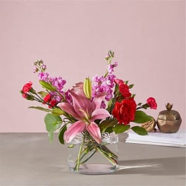 Pink lily and red carnation arrangement in a clear glass vase