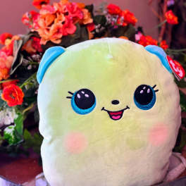 Plush smiling character pillow in front of orange flowers