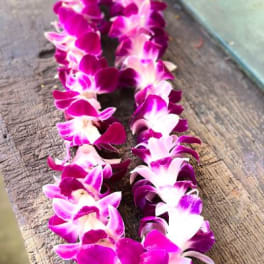 Two purple and white orchid leis laid on a wooden surface.