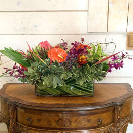 Tropical flower arrangement in a rectangular glass vase with orange and purple blooms