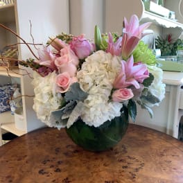 Pink lilies and roses arranged with white hydrangeas in a green glass vase.