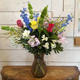 Mixed bouquet of roses, lilies, and blue delphinium in a glass vase