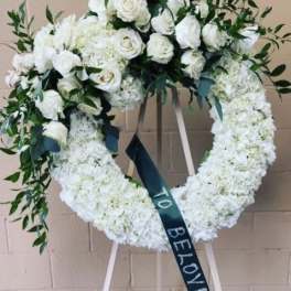 White floral funeral wreath on an easel with a memorial ribbon