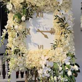 Large white floral clock display with roses and orchids