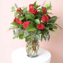 Red roses arranged in a clear glass vase with greenery
