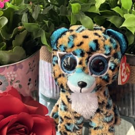 Plush leopard toy beside red roses and a potted plant