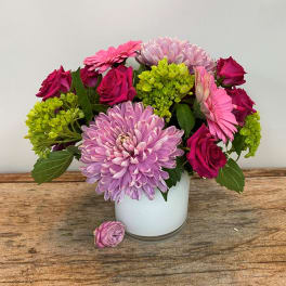 Pink roses, gerbera daisies, and lavender mum in a white vase on a wooden surface