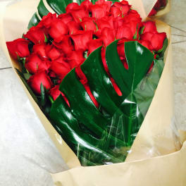 Bouquet of red roses wrapped in tan paper with glossy green leaves